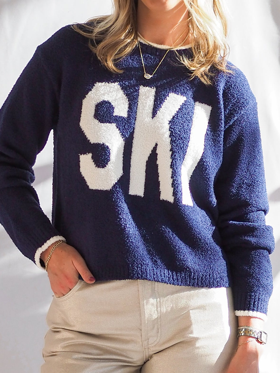 Person wearing a navy sweater with &#39;Ski&#39; text, standing next to decorative items on a table.