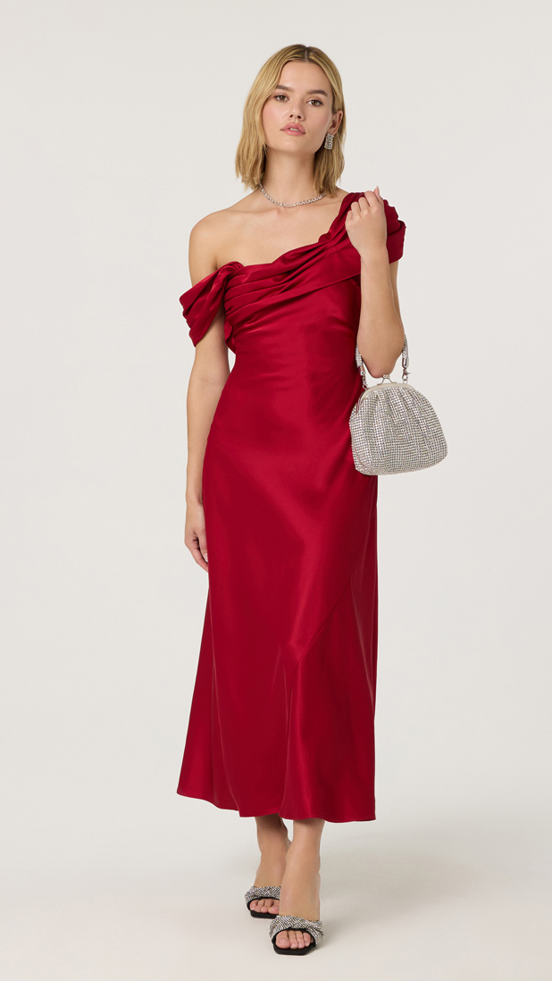 Woman wearing a red one-shoulder dress holding a silver handbag on a white background